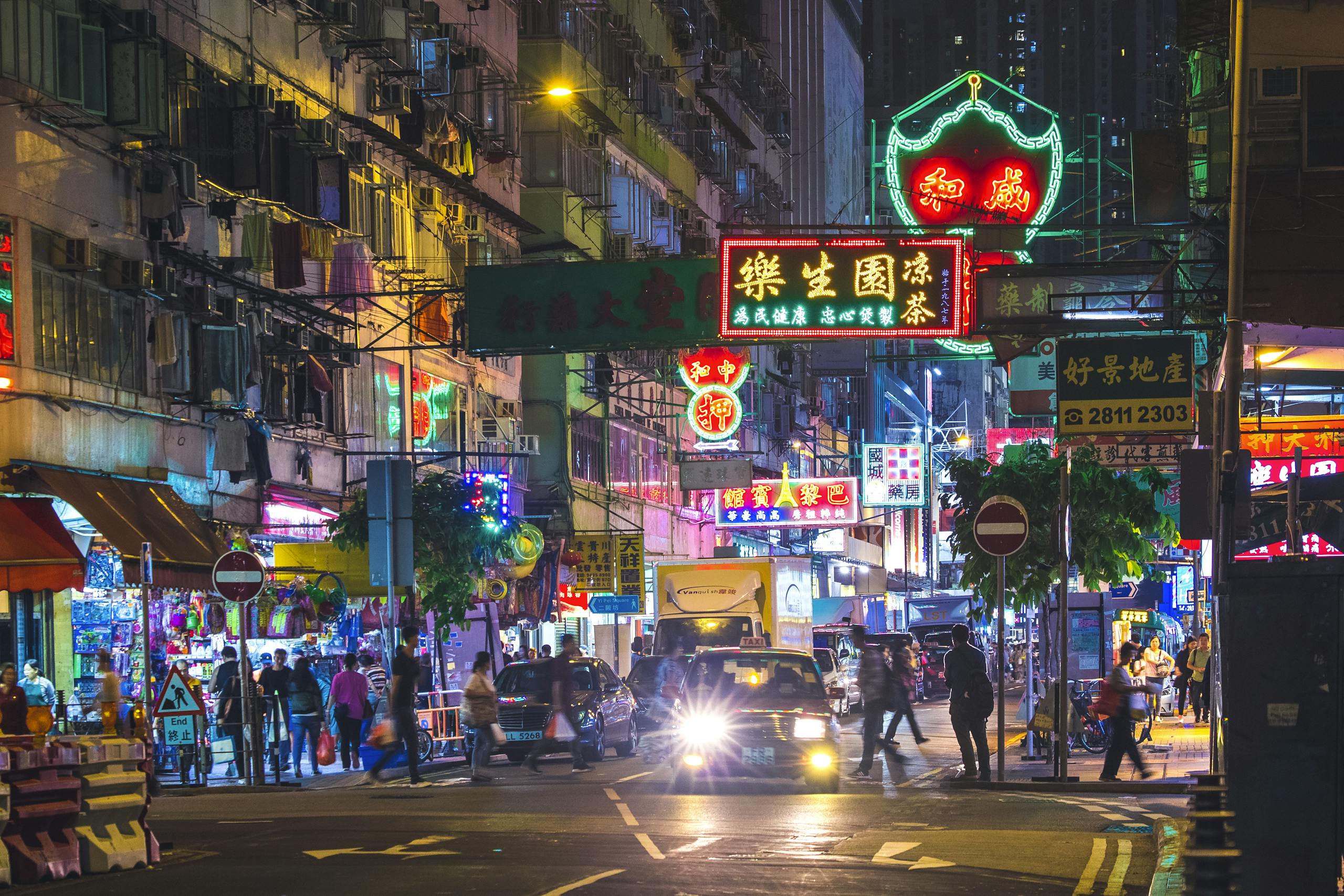 Colorful neon lights illuminate a bustling street in the New Territories, Hong Kong, by night.